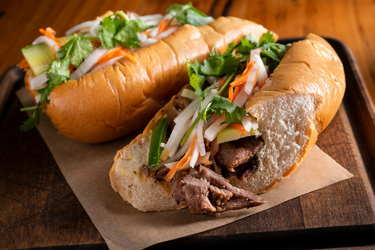 pics - 1 A freshly made Bánh Mì sandwich filled with grilled meat, pickled vegetables, cucumber slices, cilantro, and chili, all tucked into a crispy, golden-brown baguette.