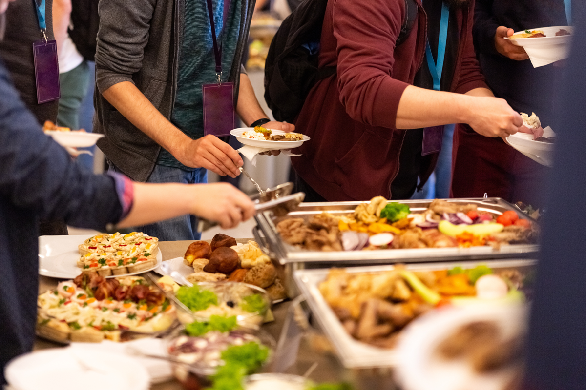 buffet table Guests serving themselves from a buffet table filled with a variety of hot and cold dishes.